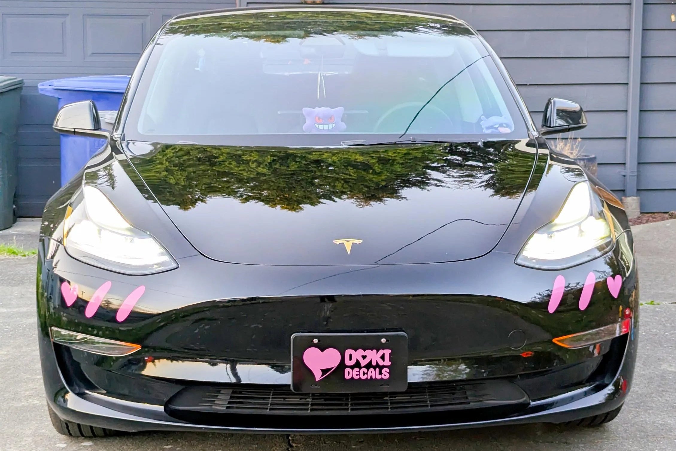 Black Tesla car with pink decorations in front of a gray garage.