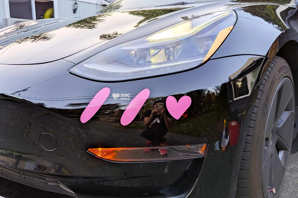 Black car with pink heart stickers on a driveway
