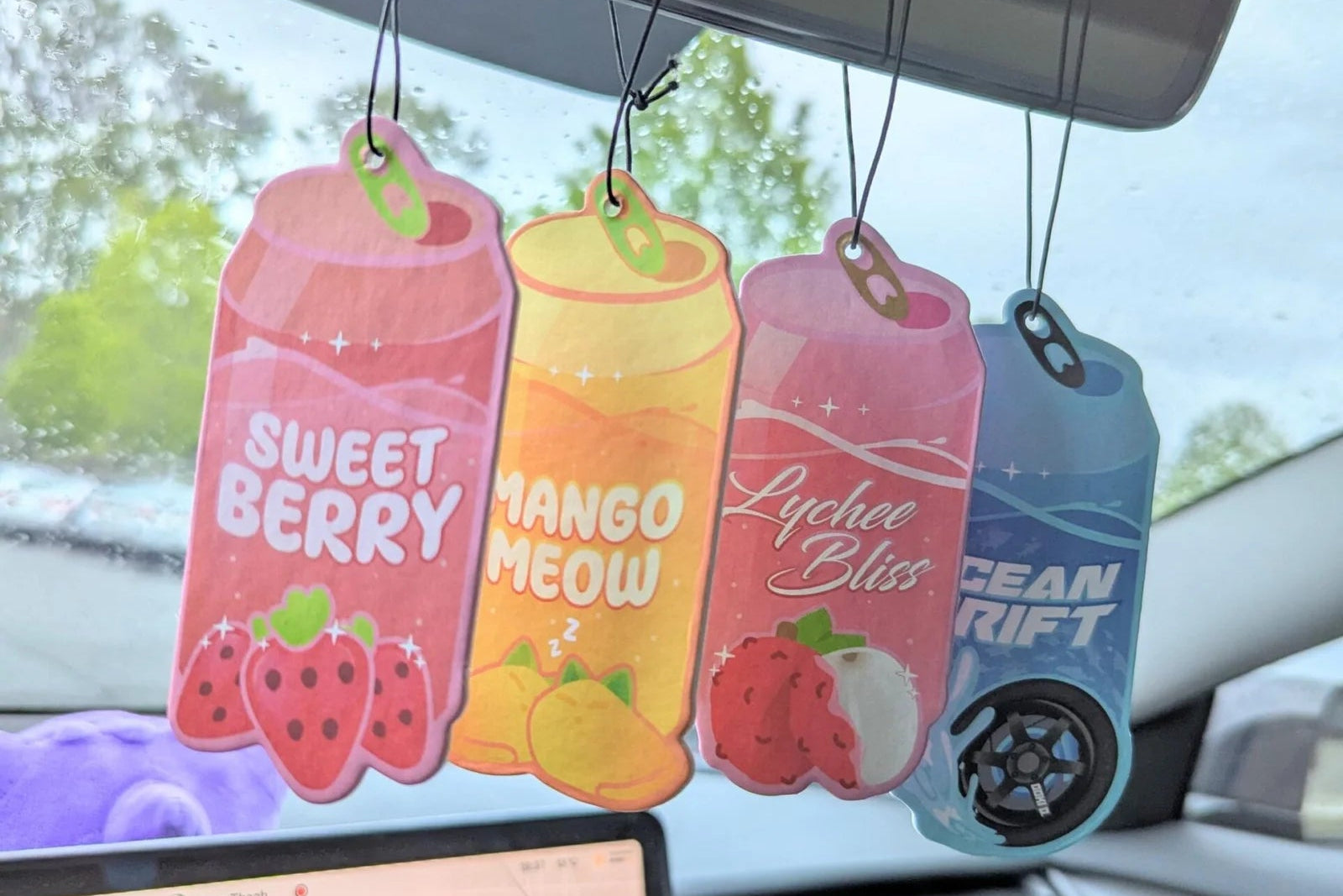 Car air freshener hanging from a car's rearview mirror with colorful packaging.